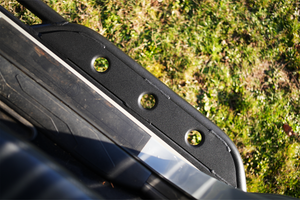 Close-up of black metal rock slider with three circular holes installed on 2016 Tacoma short bed 4-door truck.