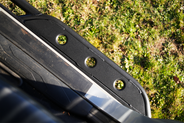 Close-up of black metal rock slider with three circular holes installed on 2016 Tacoma short bed 4-door truck.