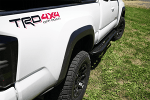 Close-up of black Metal Tech 4x4 sliders installed on white 2016 Tacoma Access Cab 1.5 door truck on grass.