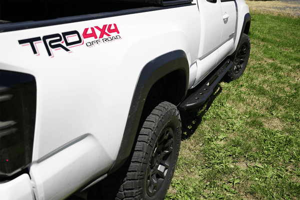 Close-up of black Metal Tech 4x4 sliders installed on white 2016 Tacoma Access Cab 1.5 door truck on grass.
