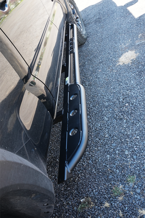 Black metal rock slider installed on the side of a 2016 Tacoma 4-door long bed, shown from an angled top view.