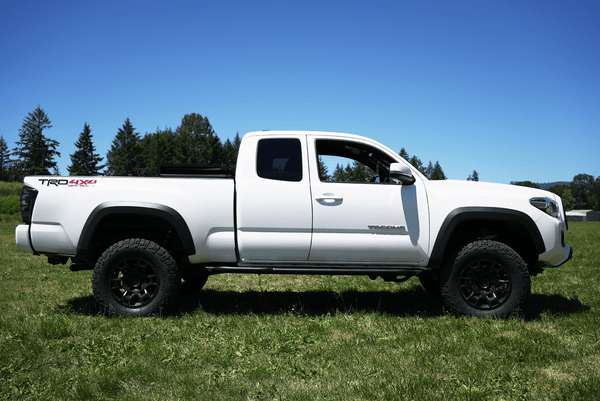 White 2016 Toyota Tacoma Access Cab with Metal Tech 4x4 black side sliders installed, shown in grassy field.