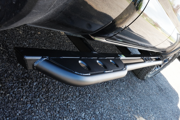 Close-up of black metal rock slider installed on side of 2016 Toyota Tacoma 4-door longbed truck.
