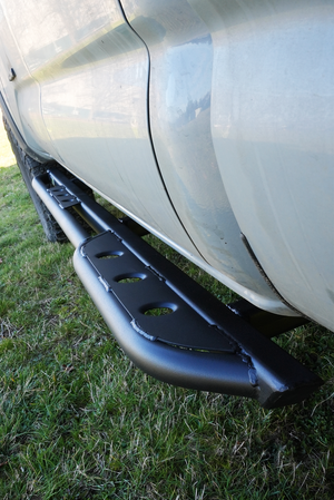 Close-up of black metal rock slider installed on the side of a 2016 Tacoma short bed 4-door truck.