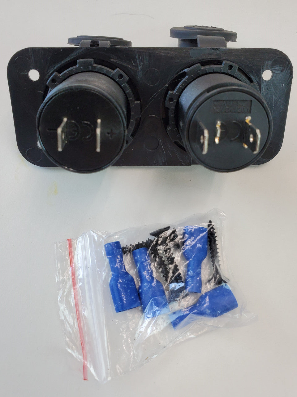 Black dual 12V power and USB plug panel with mounting screws and blue wire connectors in plastic bag.