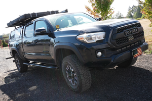 Black 2016 Toyota Tacoma 4-door longbed with Metal Tech rock sliders installed on gravel driveway.