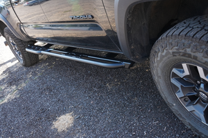 Black metal rock slider installed on the side of a black 2016 Toyota Tacoma 4-door long bed truck.