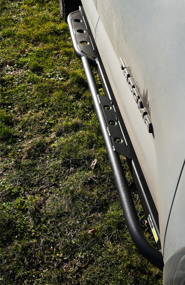 Close-up of black Metal Tech 4x4 rock slider installed on 2016 Tacoma short bed, showing textured finish and mounting brackets.