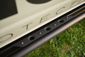 Close-up of sniper gray cerakoted step plate mounted on vehicle side rail with grass background.