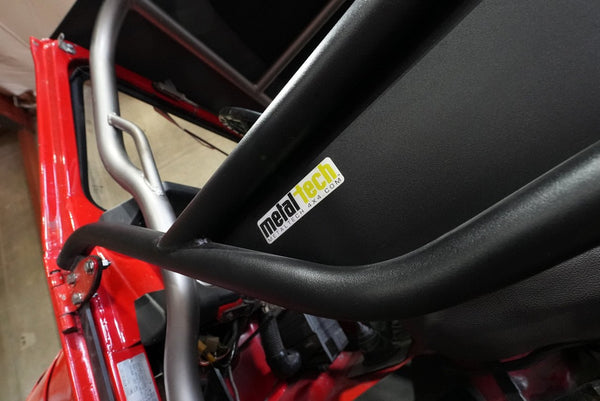 Close-up of black Metal Tech tube door installed on red FJ40 Land Cruiser showing welded frame and logo sticker.