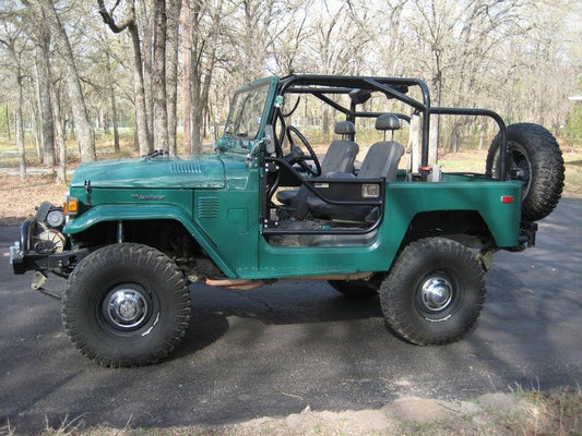 Green FJ40 Land Cruiser with Metal Tech Jackson pre-built roll cage, open doors, and off-road tires side view.