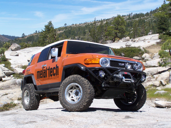 Orange FJ Cruiser with Metal Tech front tube bumper and winch mount system, shown off-road on rocky terrain.