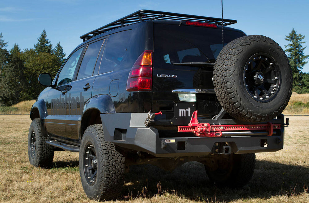 Off-road vehicle with installed Metal Tech Stage 1 rear bumper shell, spare tire, and fuel cans on rocky terrain.