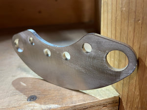 Close-up of a metal swing arm pivot plate with five mounting holes, resting on a wooden surface.