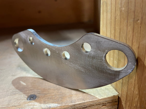 Close-up of a metal swing arm pivot plate with five mounting holes, resting on a wooden surface.