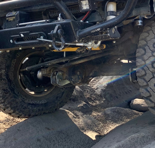 Underside view of FJ80 Land Cruiser front axle with caster correction plates installed on rough rocky terrain.