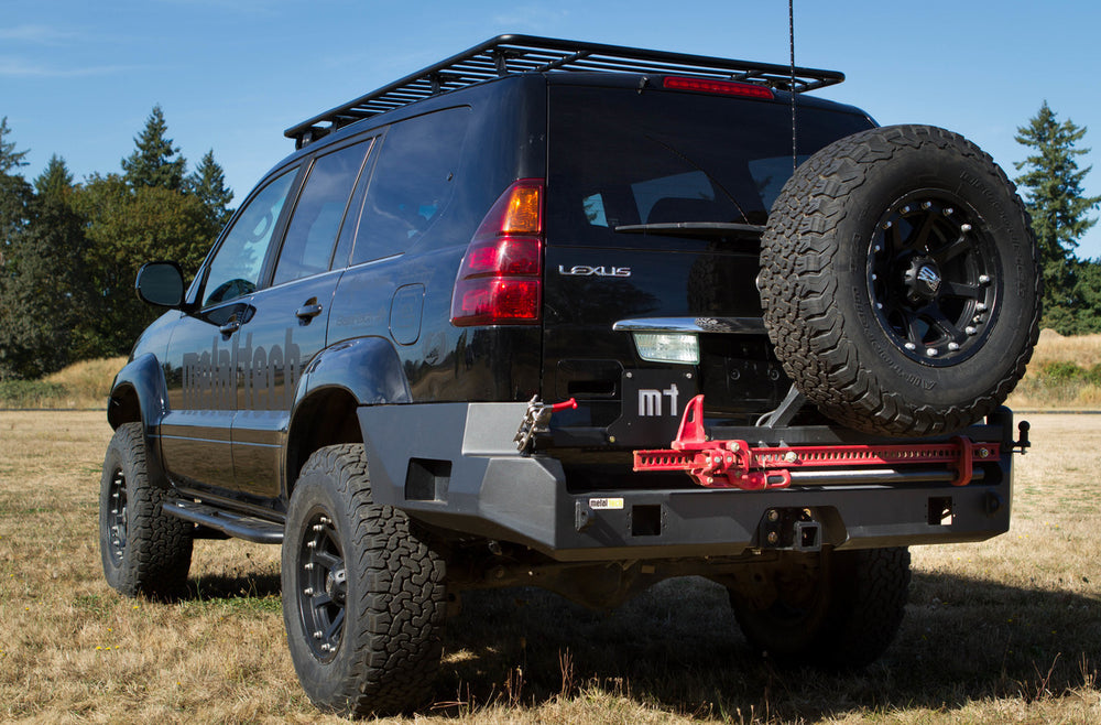 Close-up of black metal license plate holder with cutout "mt" mounted on rear swing-out bumper.