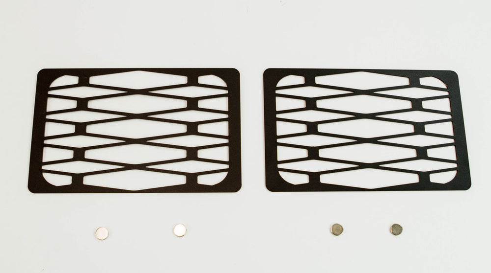 Pair of black metal tech winch hole covers with geometric cutouts for Fortress bumper, shown flat on white background.