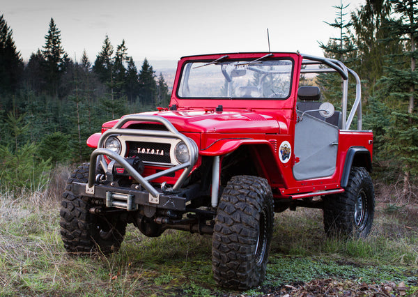 Red Toyota FJ40 Land Cruiser with installed full-profile metal roll cage and off-road tires in forest setting.