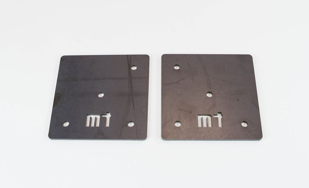 Pair of square metal front mounting plates with bolt holes and "mt" cutout for FJ40 Land Cruiser roll cage.