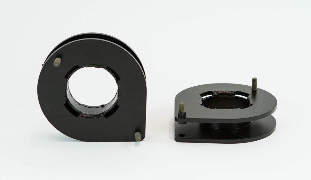 Close-up of a metal front spacer plate with welded center ring and mounting holes on a textured surface.