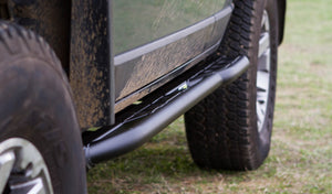 Close-up of black metal rock slider installed on side of muddy 4x4 FJ Cruiser near rear tire.