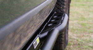 Close-up of black Metal Tech 4x4 rock slider installed on side of FJ Cruiser near rear tire outdoors.