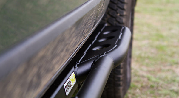 Close-up of black Metal Tech 4x4 rock slider installed on side of FJ Cruiser near rear tire outdoors.