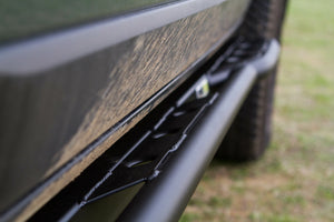 Close-up of black metal rock slider installed on side of FJ Cruiser with dirt on vehicle body.