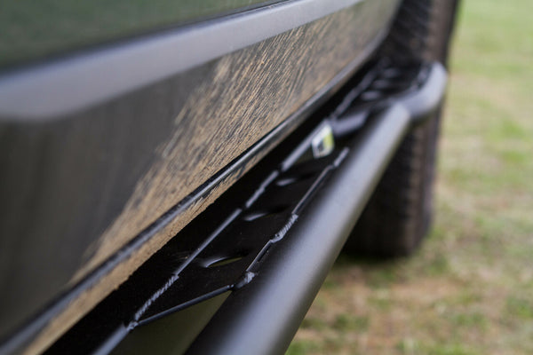 Close-up of black metal rock slider installed on side of FJ Cruiser with dirt on vehicle body.