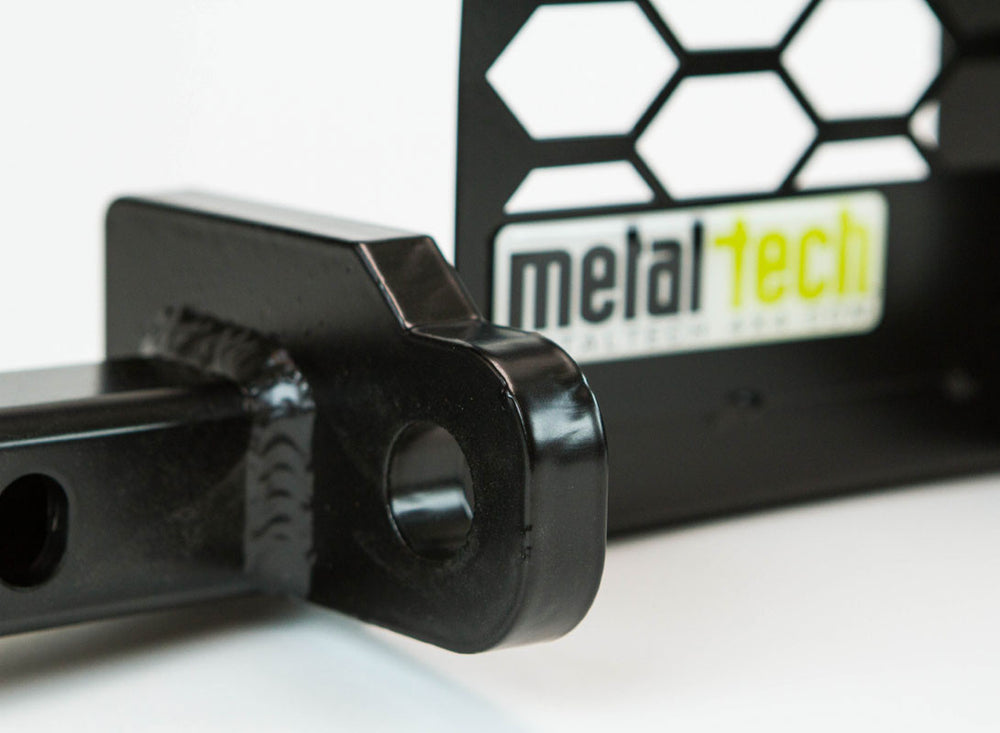 Close-up of black metal winch mount bracket with hex-patterned backing, designed for FJ Cruiser front tube bumper.