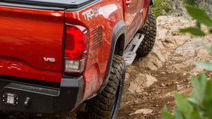 Close-up of metal rock sliders installed on a red 2016 Tacoma short bed 4-door off-road truck on rocky terrain.