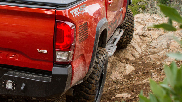 Close-up of metal rock sliders installed on a red 2016 Tacoma short bed 4-door off-road truck on rocky terrain.
