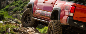 Red 2016 Tacoma 4-door with Metal Tech 4x4 rock sliders installed on rocky off-road terrain.