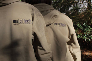Close-up of two tan Metal Tech 20th Anniversary Tactical Jackets showing embroidered logo on upper back and sleeve patch area.