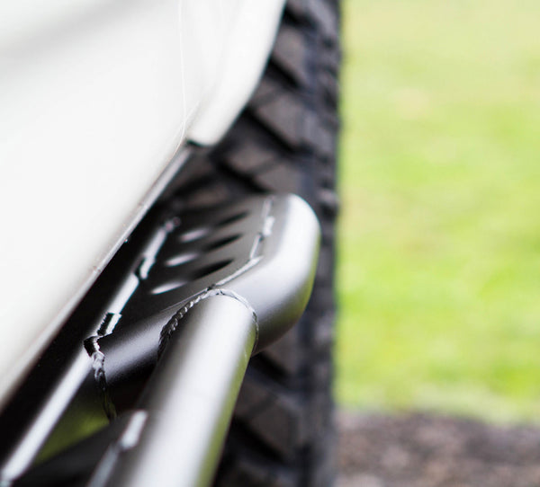Close-up of black metal trail rock slider mounted on 2010 4Runner near rear tire and white body panel.