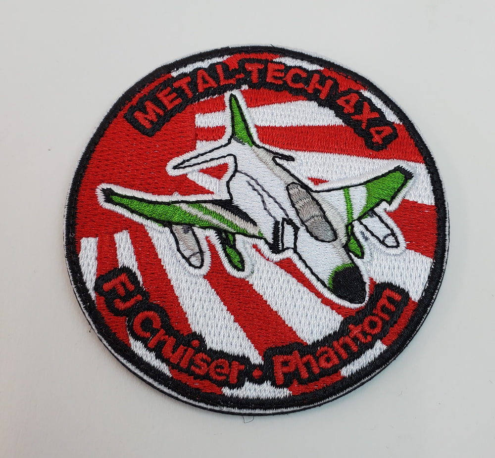 Round embroidered patch with a white and green jet on red and white rays, labeled "Metal-Tech 4x4 FJ Cruiser Phantom."