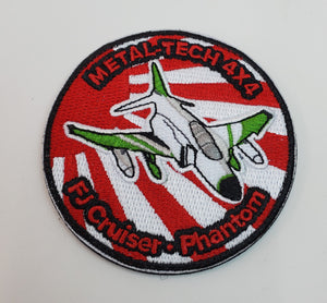 Round embroidered patch with a white and green jet on red and white rays, labeled "Metal-Tech 4x4 FJ Cruiser Phantom."