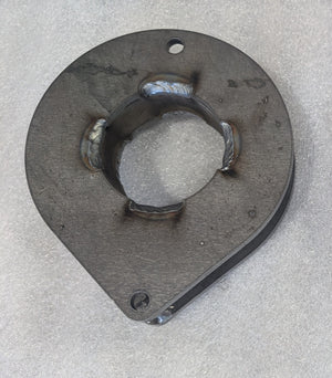 Close-up of a metal front spacer plate with welded center ring and mounting holes on a textured surface.