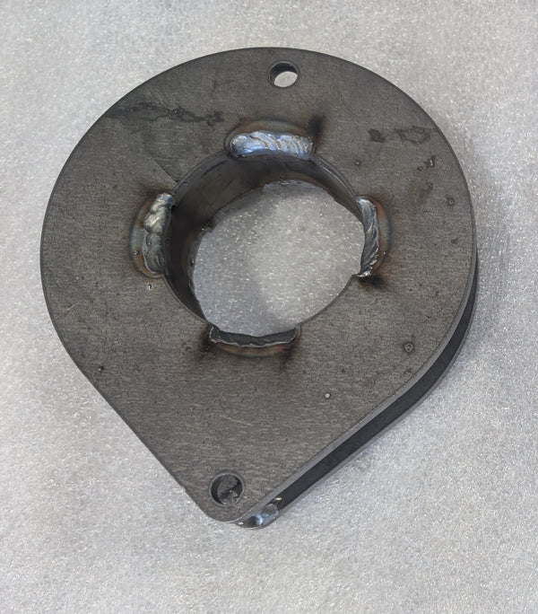 Close-up of a metal front spacer plate with welded center ring and mounting holes on a textured surface.