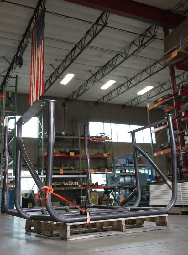 Pre-built full-profile metal roll cage for FJ40 Land Cruiser, shown upside down on a wooden pallet in a workshop.