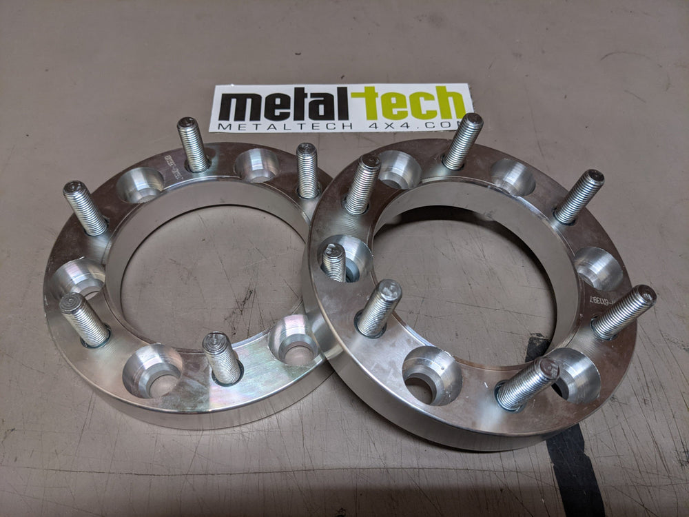 Pair of 6x5.5 1-inch hub-centric aluminum wheel spacers with studs, shown inside an open box on a work surface.