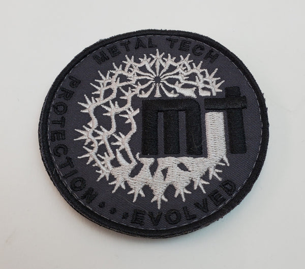 Round black and silver embroidered morale patch with "Metal Tech" text and abstract thorn design.
