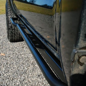 Close-up of black metal rock slider installed on 2005-2015 Toyota Tacoma side, showing textured step and mounting points.
