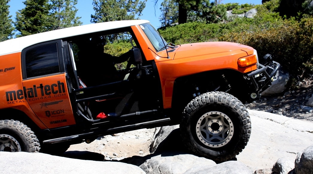 Orange FJ Cruiser on rocky terrain with 'metal-tech' branding.