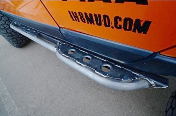 Close-up of metal rock slider installed on orange 4x4 FJ Cruiser side, showing welded steel construction and step plate holes.