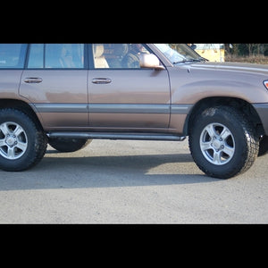 Side view of a brown 100 Series Land Cruiser LX470 with black rock sliders installed below the doors.