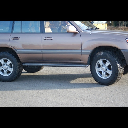 Side view of a brown 100 Series Land Cruiser LX470 with black rock sliders installed below the doors.