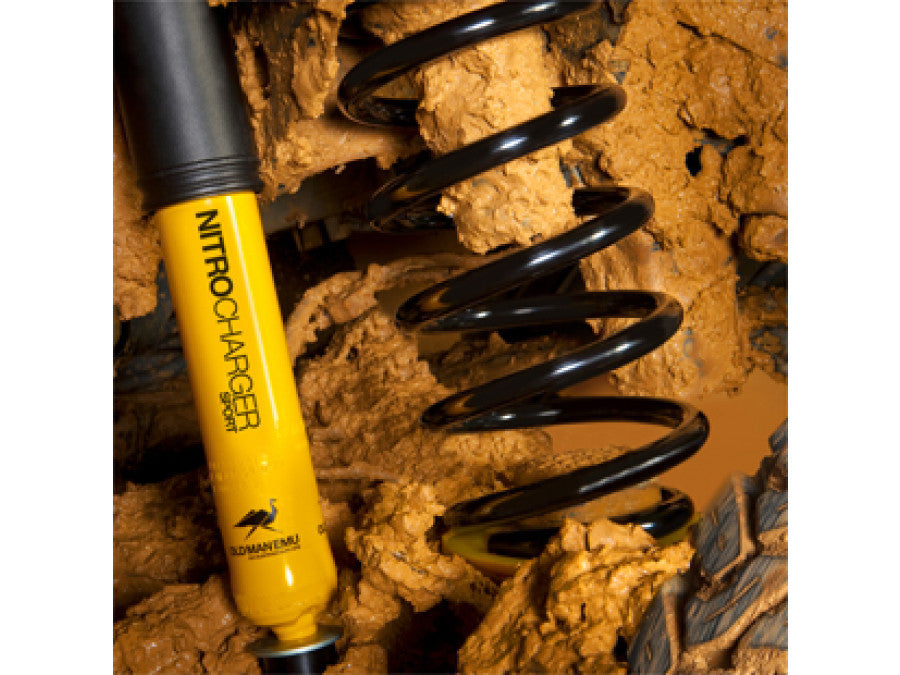 Close-up of black coil spring and yellow Nitrocharger Sport shock absorber covered in mud on Land Cruiser front suspension.