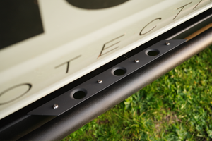 Close-up of black metal Sidewinder rock slider mounted under 2021 Bronco 4-door side panel on grass background.